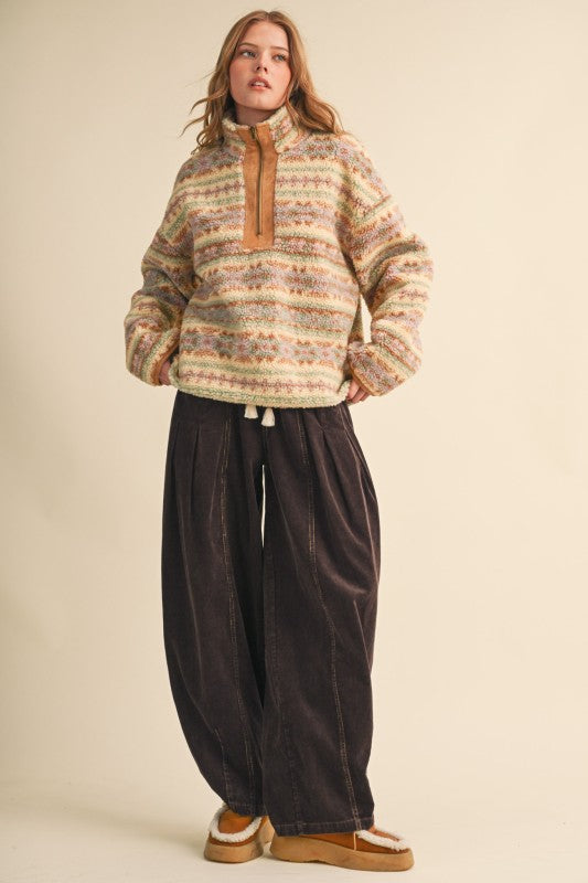 A woman modeling a fuzzy quarter-zip pullover sweater with horizontal multicolor knit stripes in beige, brown, and cream, paired with dark wide-leg pants and tan slip-on shoes against a plain beige studio background.